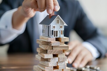 Hand Placing Mini House on Stacked Wooden Blocks, Financial Growth Concept