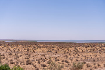 A vast, empty desert with a blue sky in the background. The sky is clear and bright, and the desert is dry and barren