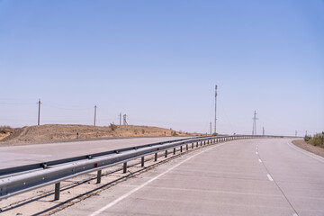 Fototapeta premium A long, empty road with a few poles and a fence. The sky is clear and blue