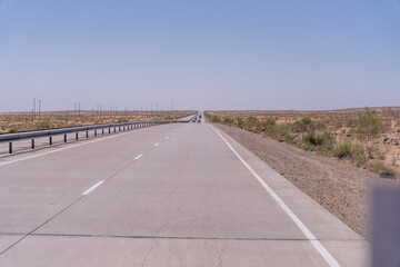 A long, empty road with no cars on it. The sky is clear and the sun is shining