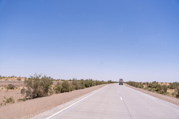 Naklejka premium A truck is driving down a road in a desert. The sky is clear and blue, and there are no clouds in sight. The scene is peaceful and quiet