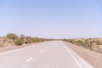 A road with no cars on it. The sky is clear and blue. The road is empty and straight