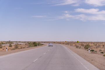 A car is driving down a road in a desert. The road is empty and there are no other cars or people in the scene. The sky is clear and the sun is shining brightly