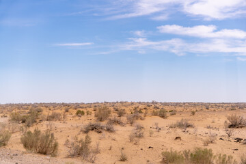 Fototapeta premium A desert landscape with a clear blue sky. The sky is dotted with clouds, and the sun is shining brightly. The scene is peaceful and serene, with the vast expanse of sand