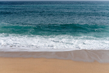Clean turquoise and blue Mediterranean or Cantabrian sea with white foam and the clean, empty sand beach in Costa Brava, Spain. 