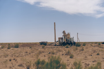 A desert landscape with a large piece of machinery in the foreground. The machinery is surrounded by a fence and a few birds are flying around it. The scene is quiet and peaceful