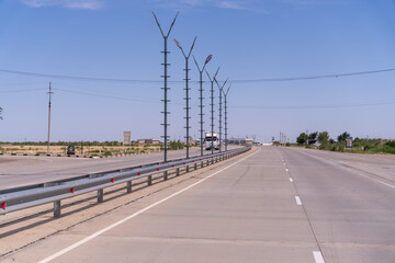 Fototapeta premium A long, empty highway with a white truck driving down it. The sky is clear and the sun is shining brightly