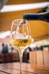 Pouring white wine into a glass on a terrace with blurred building in background