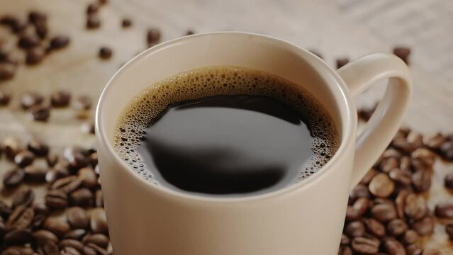 White cup of coffee on a wooden table with coffee beans and rising steam slowly rotates. Nice warm coffee background for your projects.