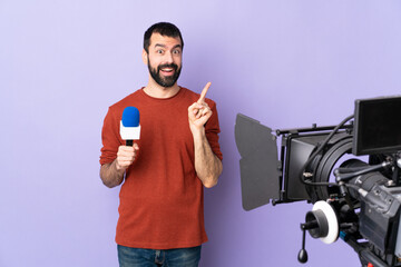 Reporter man holding a microphone and reporting news over isolated purple background intending to realizes the solution while lifting a finger up