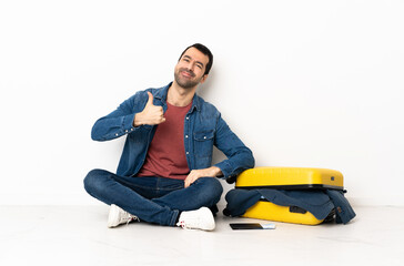 Caucasian handsome man with a suitcase full of clothes sitting on the floor at indoors giving a thumbs up gesture