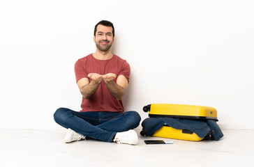 Caucasian handsome man with a suitcase full of clothes sitting on the floor at indoors holding copyspace imaginary on the palm to insert an ad