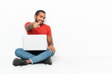 Young Ecuadorian man with a laptop sitting on the floor isolated on white background points finger at you with a confident expression