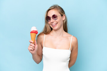Young blonde woman in swimsuit holding an ice cream isolated on blue background with happy...