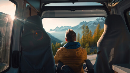 A person sits inside a van, admiring the golden-hour light over a mountainous landscape outside.