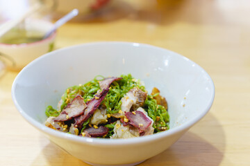 Green tea egg noodle with pork wonton, red roasted pork and crispy pork in a bowl. Fusion food add antioxidant from green tea on egg noodle. Selective focus. Chinese food.