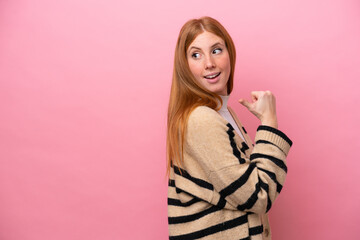 Young redhead woman isolated on pink background pointing to the side to present a product