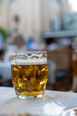 A glass of beer sits on a table in front of a person. The glass is half full and the beer is foamy. The scene is casual and relaxed, with the person likely enjoying a drink with friends or family