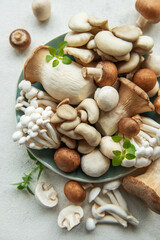 Assortment of various raw mushrooms on gray concrete background.
