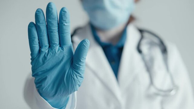 In a medical setting, a healthcare worker in protective gear advises caution and safety during the pandemic with a stop gesture. Key topics include health, coronavirus, and quarantine