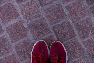 A pair of red shoes are standing on a brick floor. The shoes are the only thing visible in the image