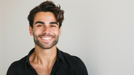 Obraz premium A young man with a light beard and tousled hair smiles warmly, exuding confidence against a neutral background.