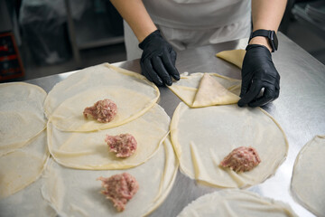 Kitchen worker forms empanadas with meat filling