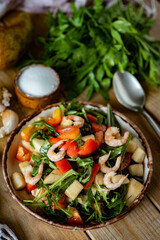 Salad with shrimp, arugula, fresh tomatoes and olive oil in a beautiful plate on wooden boards. A breakfast dish. Vertical photo. Close-up