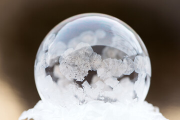 A frozen bubble in the snow with bokeh in the background. Beautiful frosty patterns on a frozen soap bubble. winter, frosty background. Frozen bubble at sunset light. soap bubble on snow close up