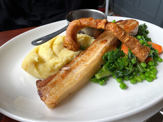 British food, pork belly elegantly served on the plate with greens, carrots, potato mash and gravy