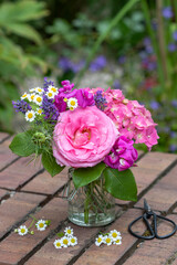 Blumenstrauß mit pink Rose, Hortensienblüten, Wicken, Lavendel und Mutterkraut in Glasvase im Garten