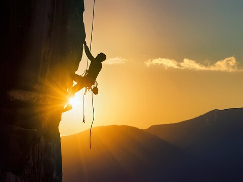 Silhouette of a Climber Scaling a Mountain at Sunset