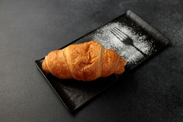 Crispy hot croissant on a black rectangular plate on a gray background