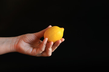 Close-up of a woman's hand holding a ripe lemon. Yellow lemon in hand on a black background....
