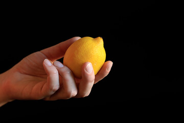 Close-up of a woman's hand holding a ripe lemon. Yellow lemon in hand on a black background....