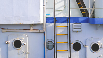 Row of porthole windows with black metal ladder of white nautical vessel
