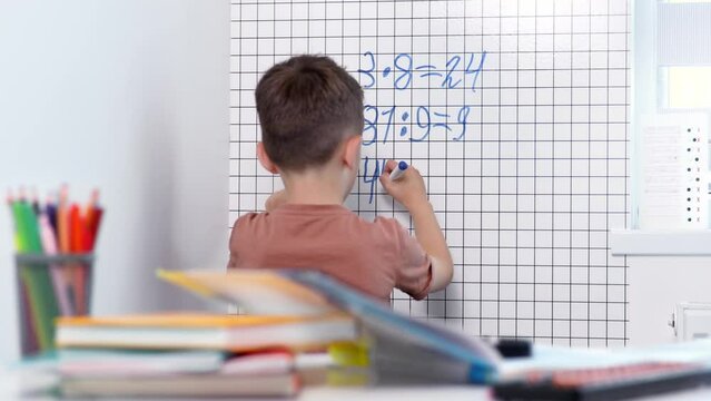 Rear view of young boy solving math problems on white board.