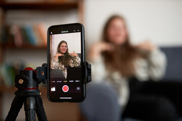 Selective focus on smartphone screen recording plus size blogger influencer on couch streaming live...