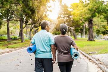 Retired couple with active lifestyle walk through the park in sportswear and on their mats after a pilates class.