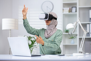 A young Muslim woman in a hijab sits in the office at a desk, wearing a virtual mask and talking remotely via online communication.