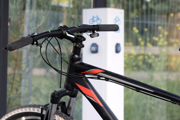 Handlebar of a traditional bicycle against the background of an electric bicycle charging station, eco-friendly urban transport, vertical.