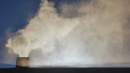 Silhouette of smoke against blue sky from the chimney of a village house.
