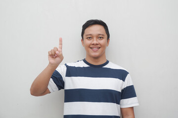 Young Asian man with striped t shirt showing one finger sign isolated on white. Male gesturing number one sign