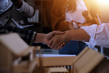 Construction team shake hands greeting start new project plan behind yellow helmet on desk in office center to consults about their building project. in sun light