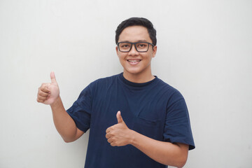 Young Asian man smiling and gesturing thumbs up isolated on white. Cheerful male wearing glasses 