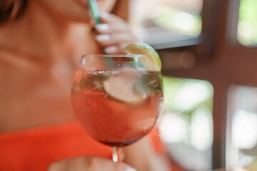 A woman is holding a glass of pink drink with a lime slice in it. Concept of relaxation and enjoyment.