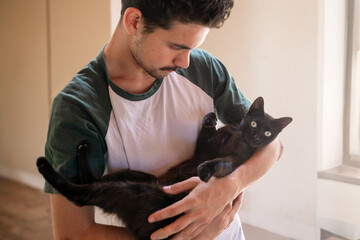 young man holds a black cat in his armas