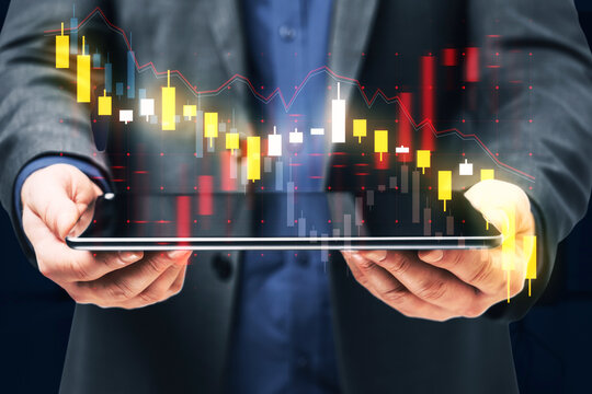 A professional businessman presenting a digital tablet with financial data and stock market graphs as part of a futuristic double exposure concept on a blurred background