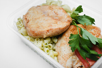 Fried chicken fillet with a side dish of pasta. Delicious meat breakfast in a container.