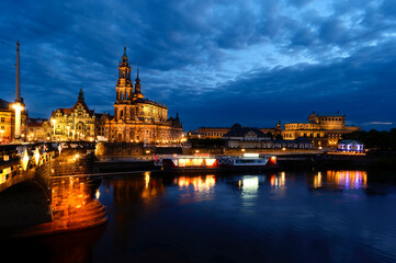 Fototapeta premium Night shot of the brightly lit historic buildings of Dresden with colorful reflections on the Elbe.